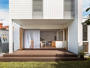 Two storey home with white panelled cladding, and a deck and lawn in the backyard.