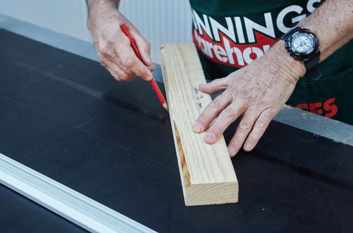 A scrap piece of timber being used as a ruler to plot out the centre of squares drawn out in a vertical garden tier for pot plants