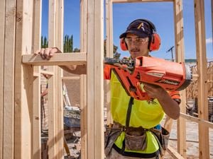A tradie uses a Paslode nail gun on a frame wearing hearing protection