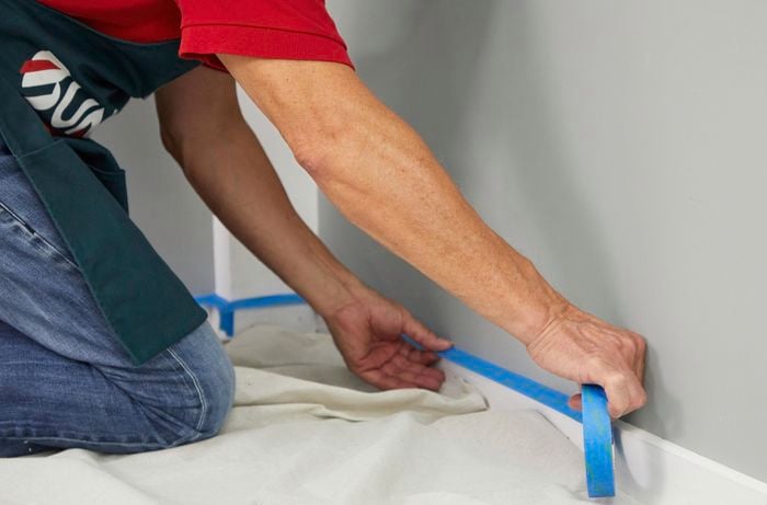 A pair of hands line interior skirting with painters’ tape.