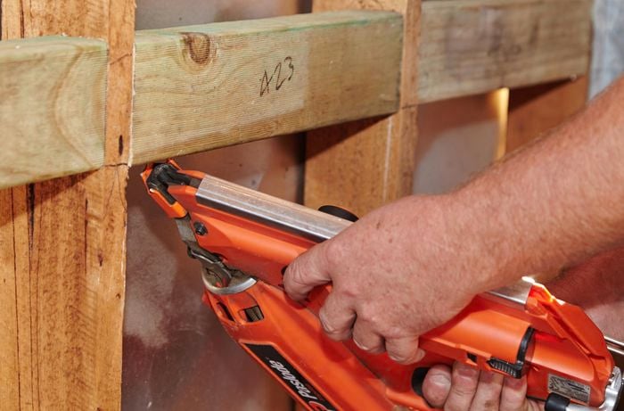 A person using a nail gun to attach a noggin between wall studs