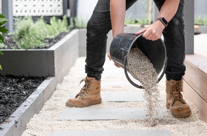 Person pouring gravel from a bucket around paving stones.