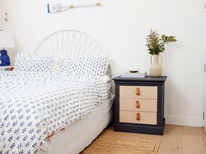 Upcycled bedside table with flower vase on top and next to a bed in the bedroom.