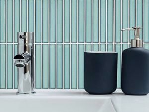 Close up of a tap and bathroom accessories with a blue pencil tiled wall.