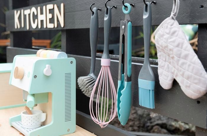 A close up of a completed outdoor play kitchen complete with plastic utensils and a play coffee machine