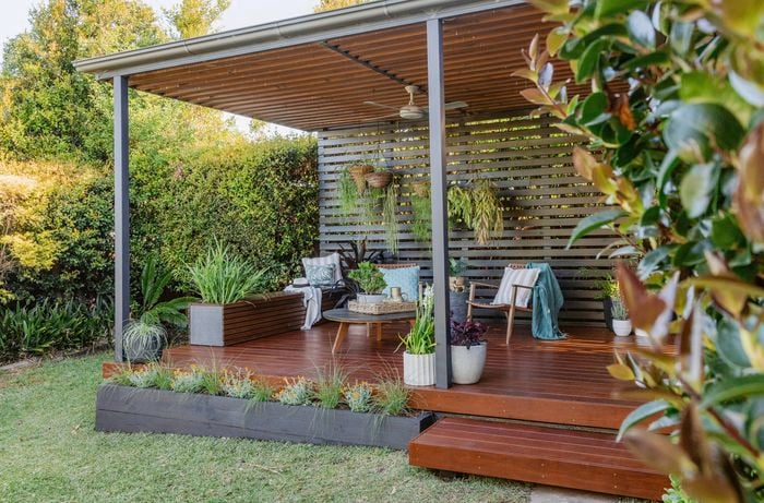 Timber deck with outdoor lounge chairs, hanging plants, and slatted privacy wall under a roof