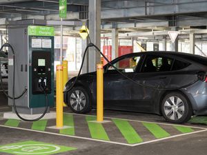 How to use a public EV charging station, demonstrated by a black Tesla parked and charging at a fast EV charger in a multi-level car park.