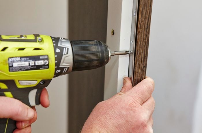 A person attaching a metal facing strip to cabinet using a cordless driver