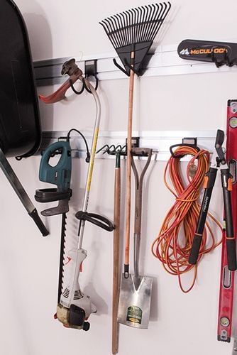 Wheelbarrow, rake, extension lead and garden tools hanging from hooks on a wall mounted rail