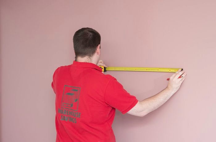 A Bunnings Team Member is measuring the width of the wall with a tape measure. 