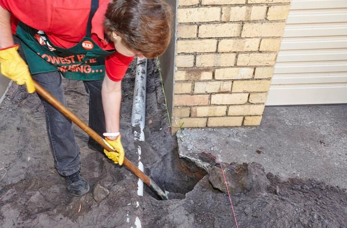 A Bunnings team member using a shovel to dig out a posthole through concrete, close to a PVC pipe