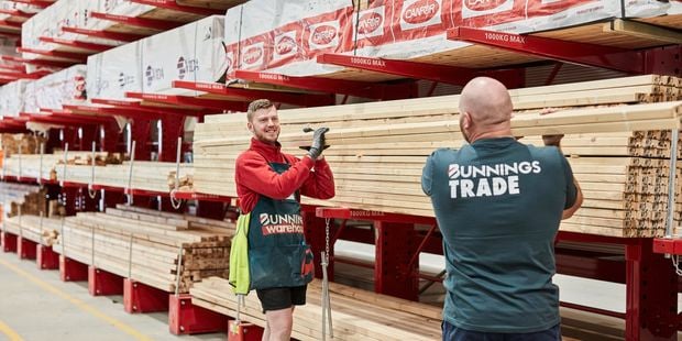 Two Bunnings team members lifting lengths of timber in the timber yard