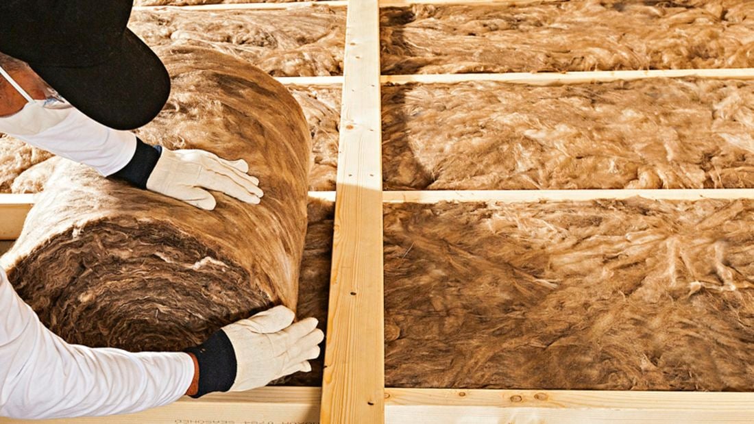 Man wearing a face mask and gloves (PPE) rolls out an insulation batt