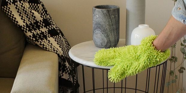 A green Sabco cleaning glove wiping down a tabletop.