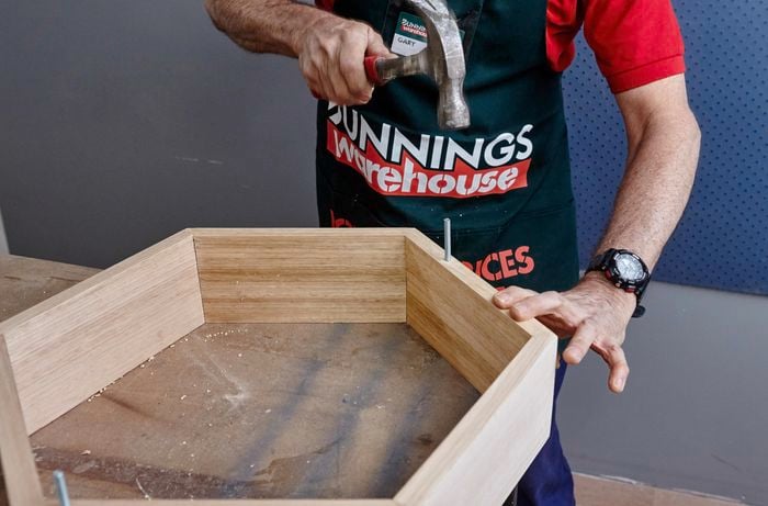 A length of dowel being hammered into a hexagonal shelf frame