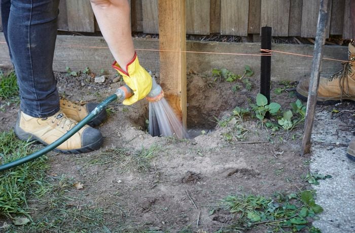A person spraying water onto concrete in a post hole