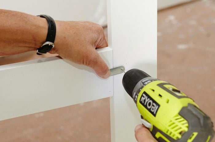 Person drilling screw into bracket on cabinet panel