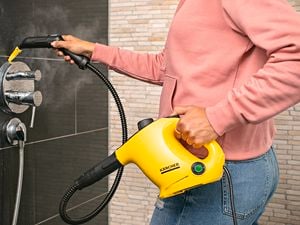 A woman uses a Kärcher steam cleaner to remove grime from a shower mixer