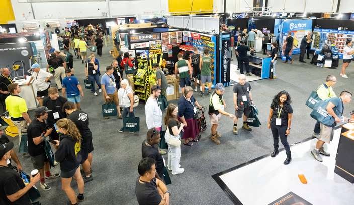 A wide view of a busy indoor trade show with attendees walking between exhibitor booths.