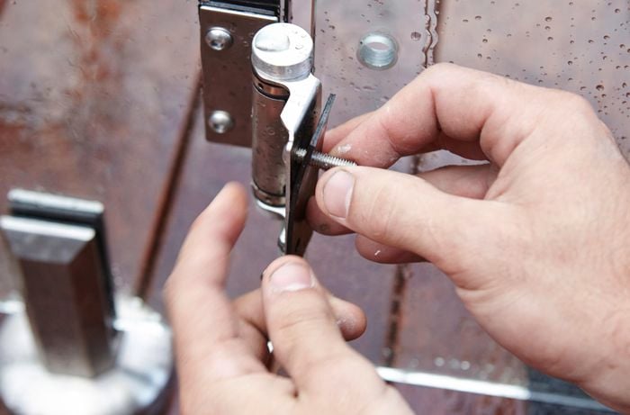 Person screwing hinge plate into pool fence gate hinge.