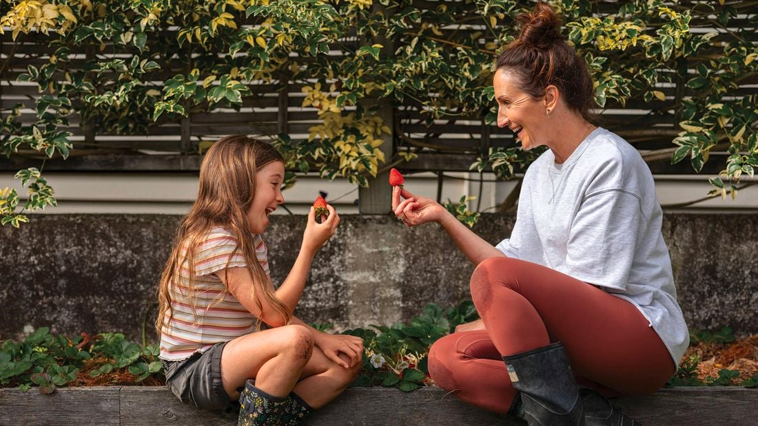 A woman and little girl holding a strawberry.