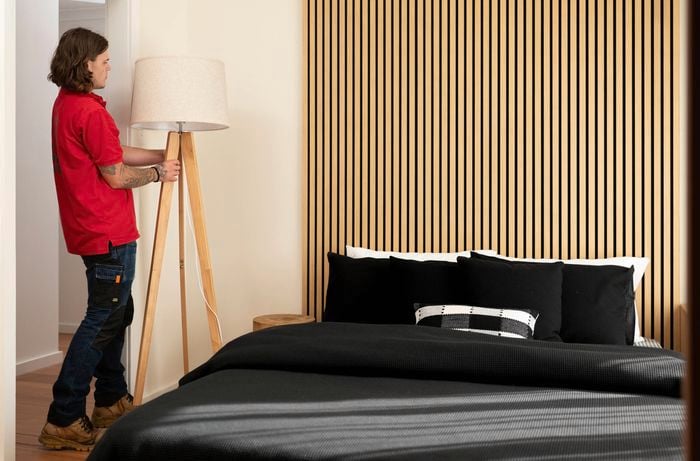 Room with a bed, floor lamp and timber panels on the walls.