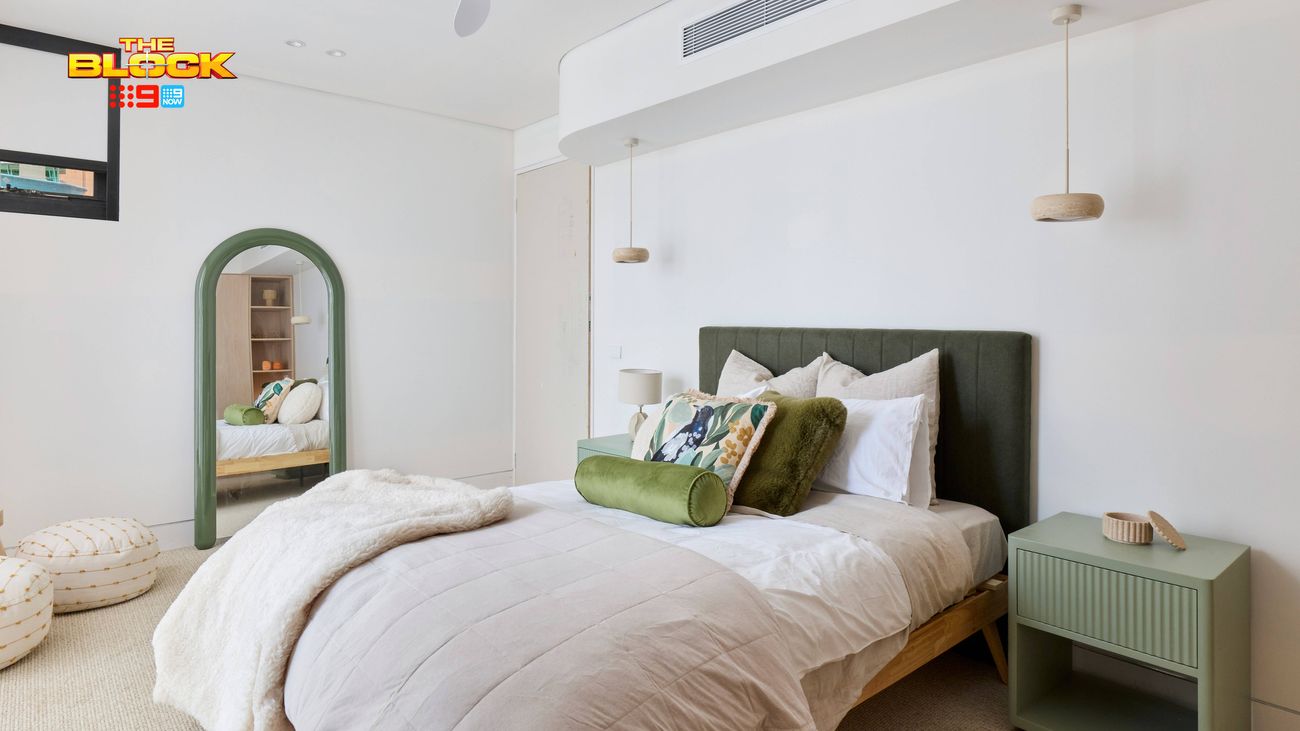 Contemporary bedroom featuring a green upholstered bedhead, neutral bedding, matching bedside table, pendant lights and an arched mirror.