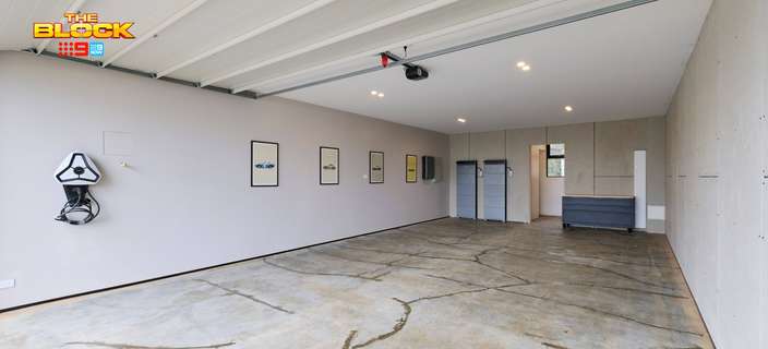 Spacious garage featuring a concrete floor, white walls, wall-mounted storage and an open roller door.