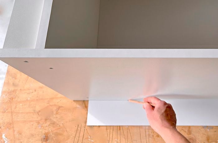 A person marks the excess material on the back of a cupboard
