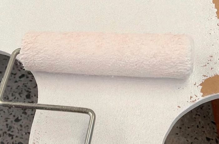 Hand using roller to apply white primer to MDF