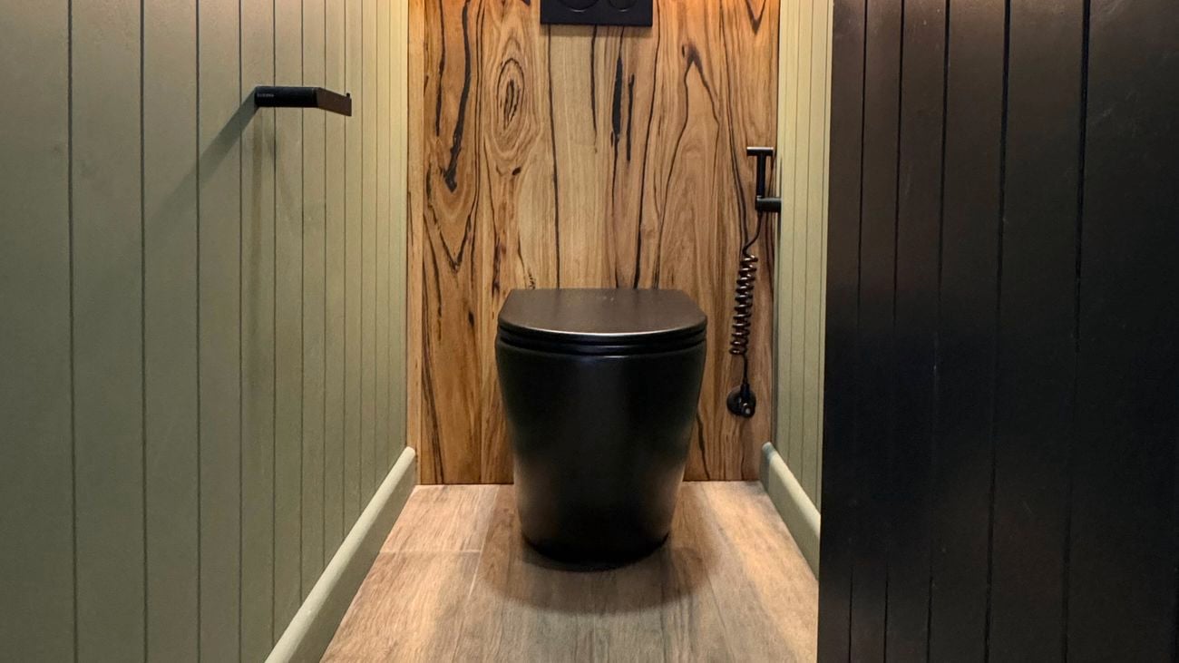 Renovated toilet with black toilet sitting on polished timber floorboards