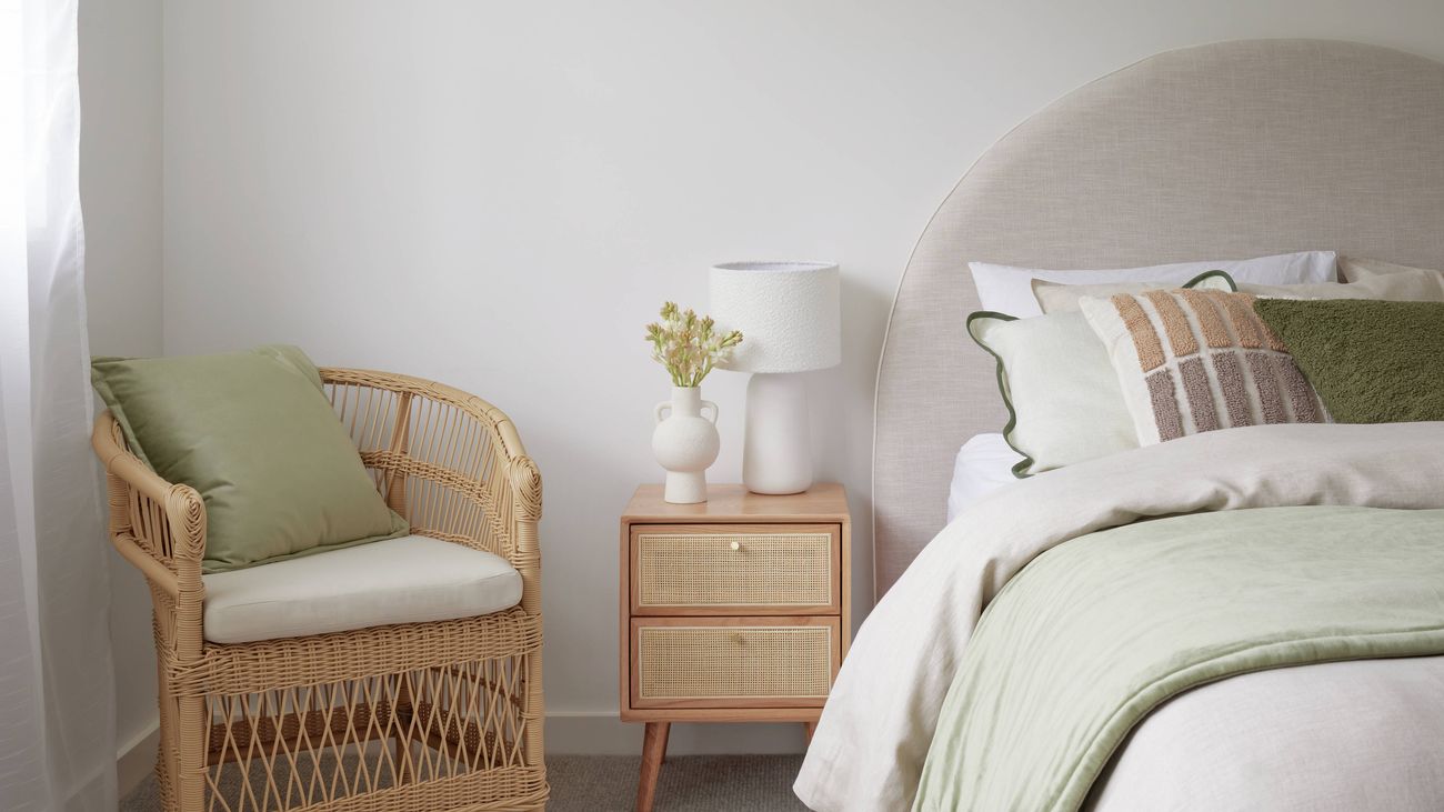 Bedroom with Rattan side sable and chair with cushions and green and white bedding