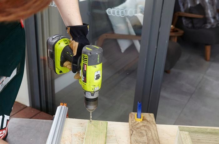 A person drilling a hole in a length of timber