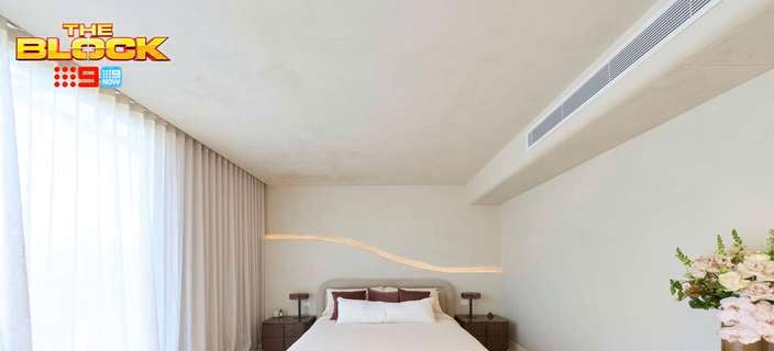 A furnished bedroom, with a be, two side tables, another table with a vase with flowers on it and carpet in the room.