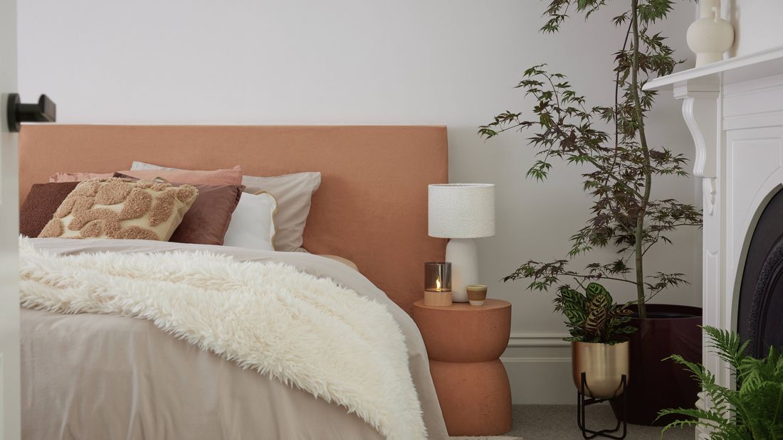 Bedroom with a large indoor plant, white lamp on side table, cushions, and white bedding