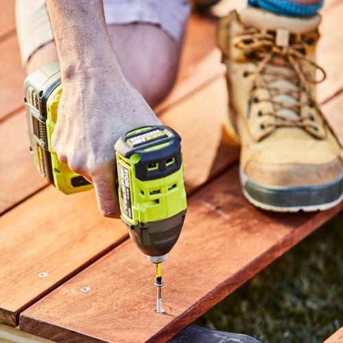 Builder drilling screws into timber planks for deck outside