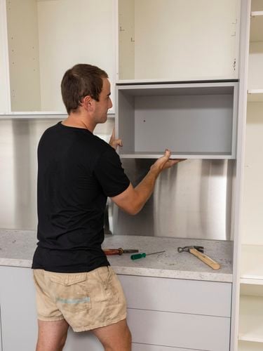Person installing or adjusting a cabinet with tools on the countertop in a kitchen or workshop setting.
