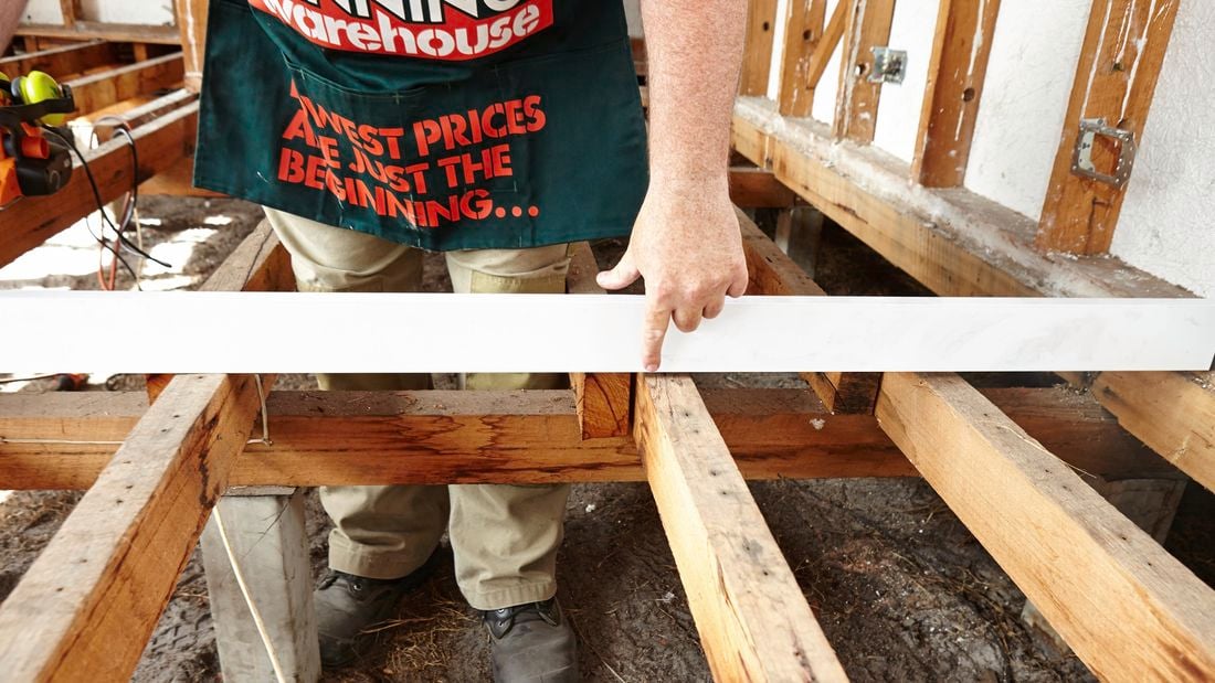 A person pointing to a gap between a floor joist and a straight edge place across it