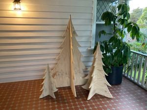 Three plywood Christmas trees of varying sizes placed on a tiled porch next to a potted plant.
