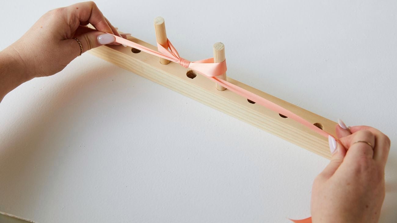 A person using a bow maker to create a bow from peach coloured ribbon.