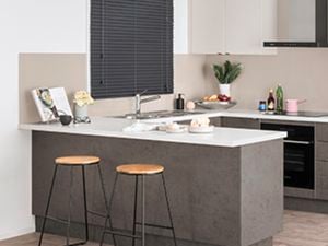 Grey themed U shaped kitchen against cream and white walls with two stools in front