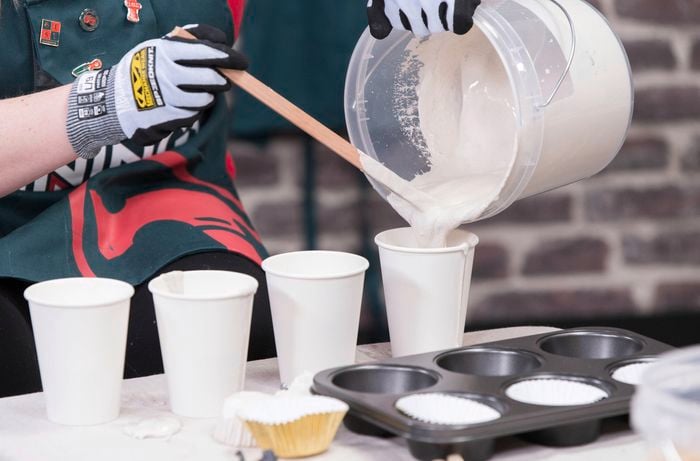  Bunnings Team Member is pouring a plaster of paris mixture from a bucket into paper cups to make the fossils.