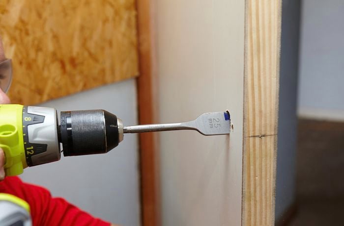 A power drill being used to create a cavity in a door for a door handle