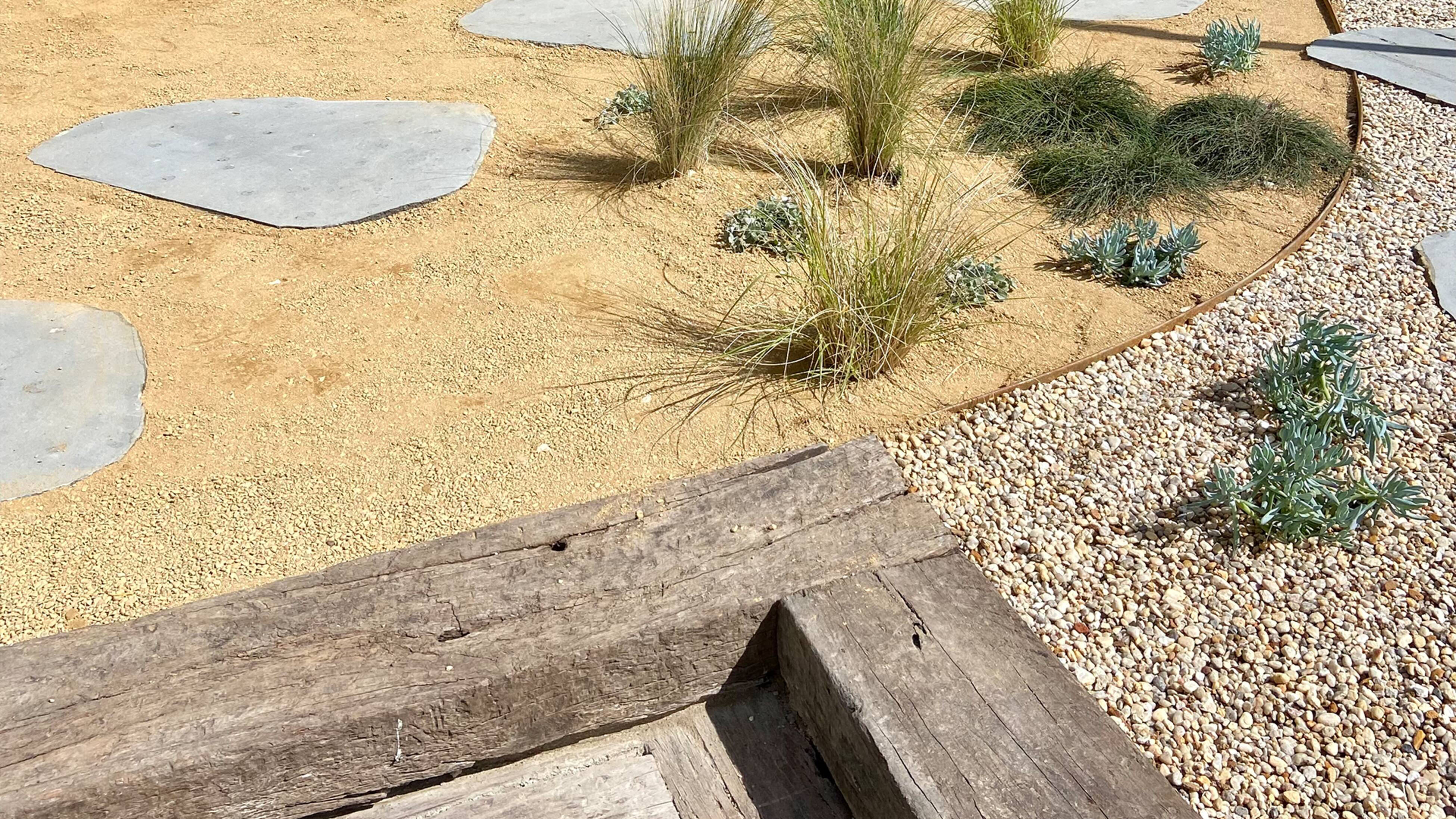 A landscaped area with various plants, stonework, sleepers and gravel