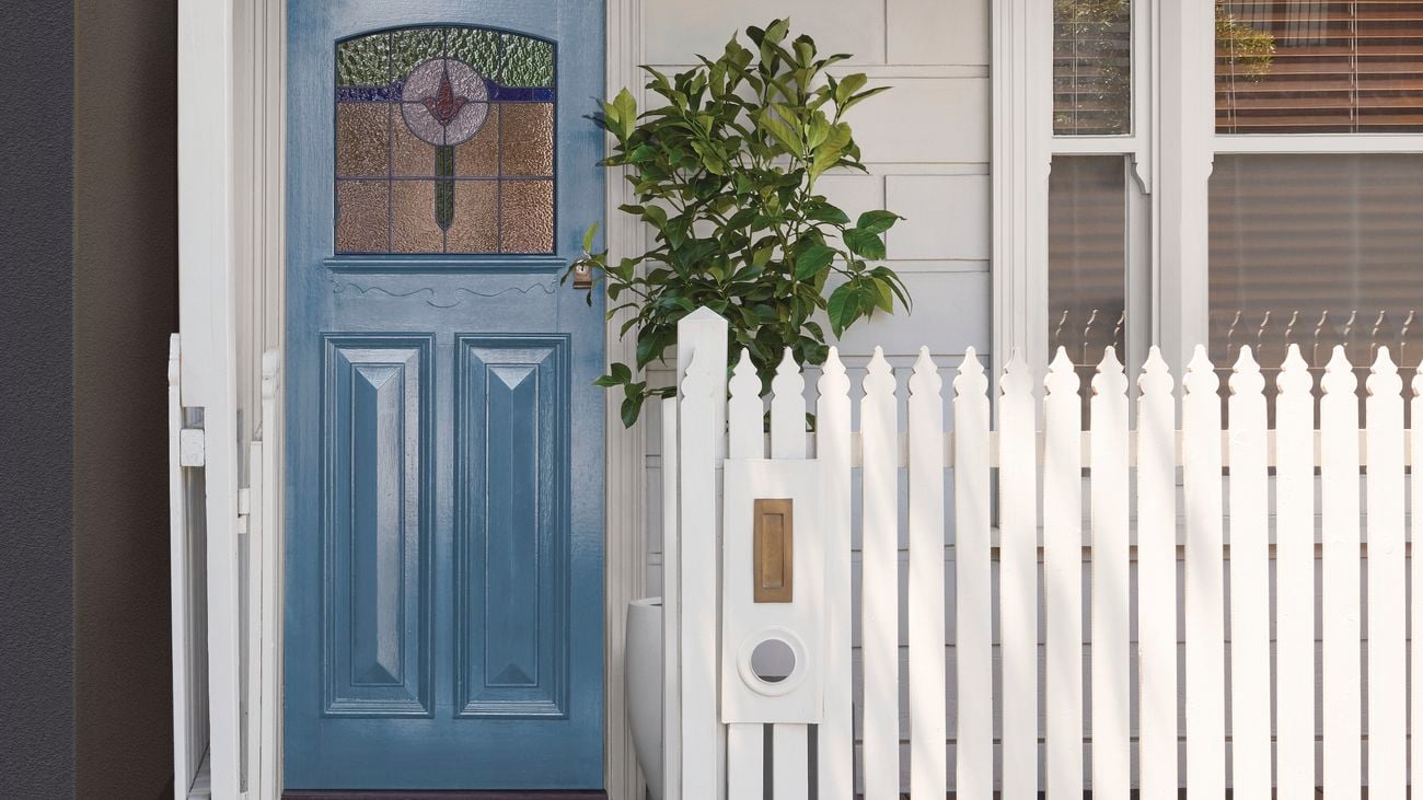 Front of a small white house with a light blue door and white picket fence.
