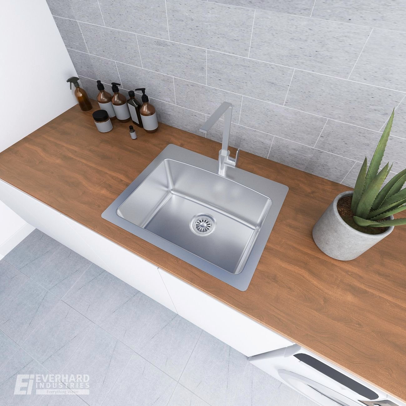 Laundry benchtop with silver sink, plant and soaps.