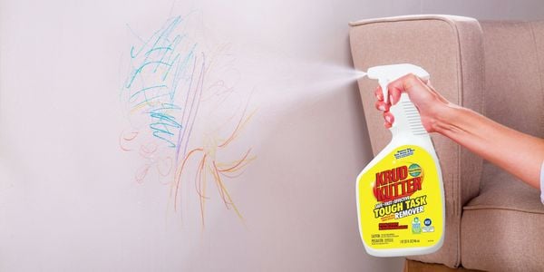 Person spraying Krud Kutter Tough Task Remover on drawings on white wall