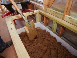 A person shovelling mortar into a timber frame for a bath