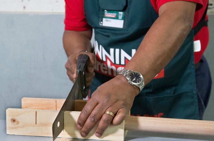 A person cutting timber using a hand saw and mitre box