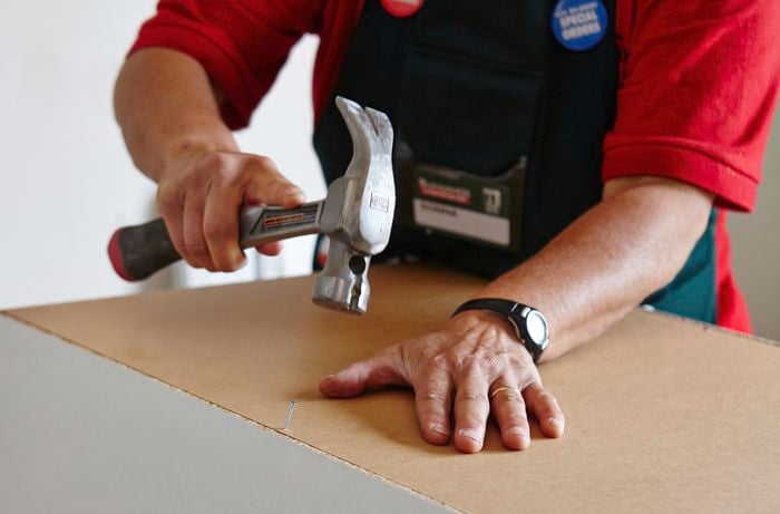 A person attaching the back panel of a cabinet using a hammer and nail